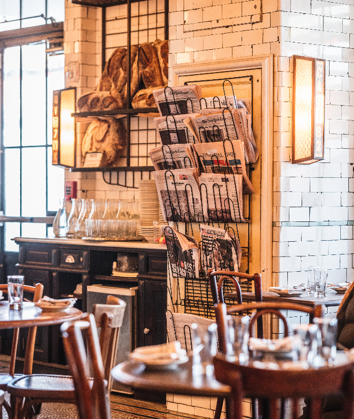 Cozy restaurant interior with wooden tables, white subway tile walls, newspaper rack, and warm lighting